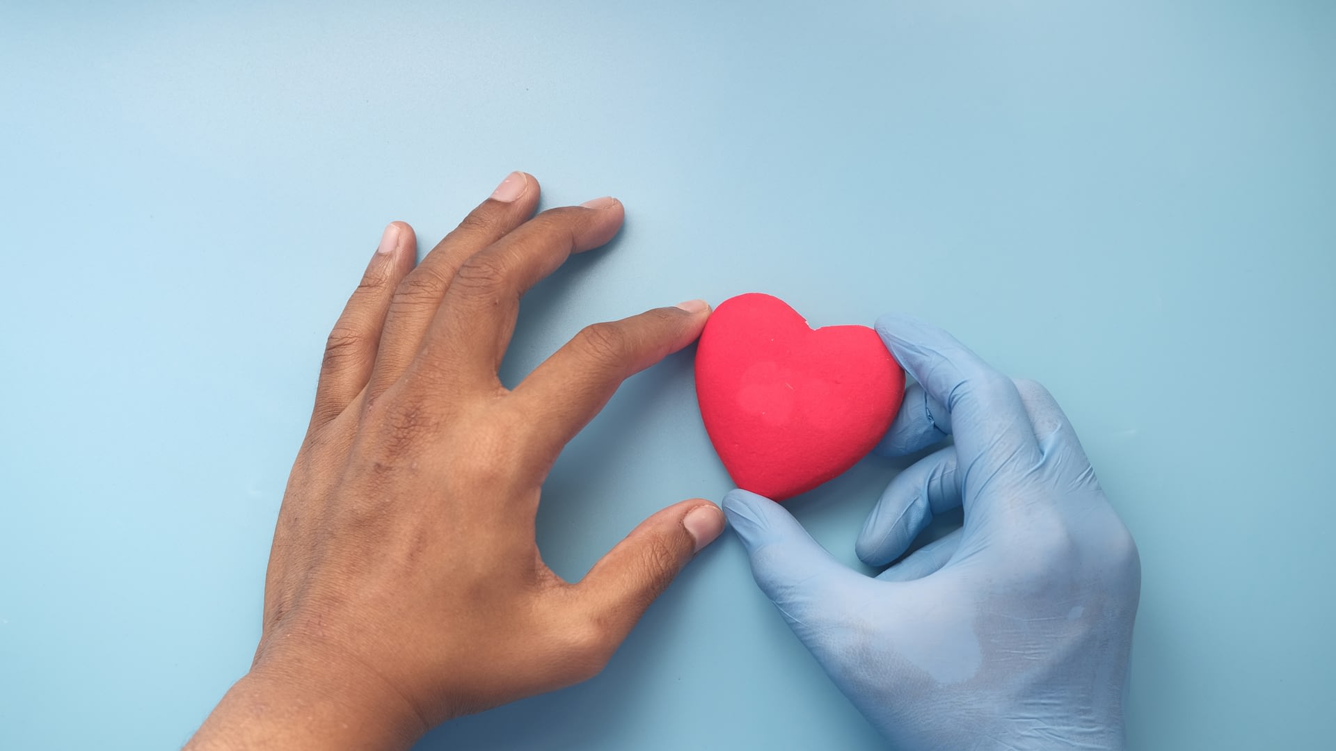 Left hand and right hand in surgical glove gently holding a toy heart.