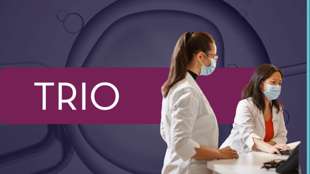 Photo of two pharmacists wearing masks and reviewing info on a computer. TRIO logo with purple background.