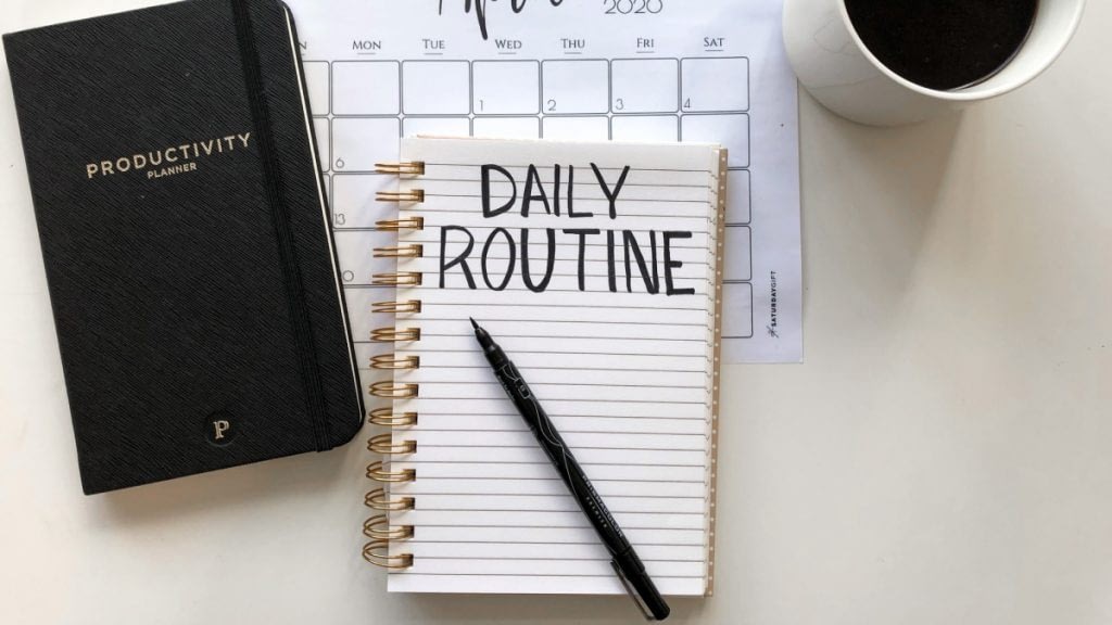 A photograph of a notebook with the text Daily Routine. Next to it is a Productivity planner.