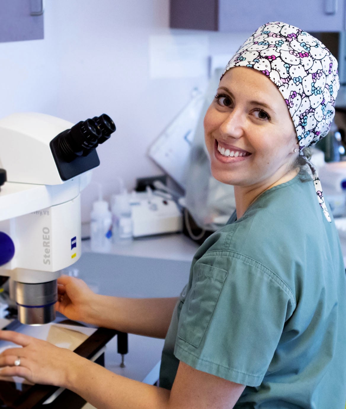A photograph of a smiling nurse sitting at a microscope in the I V F lab.