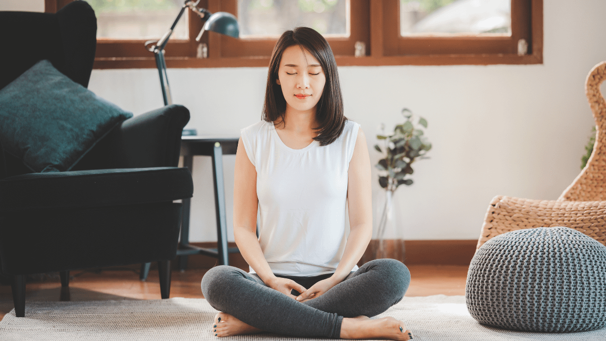 Assigned female at birth with black hair meditating with eyes closed in living room