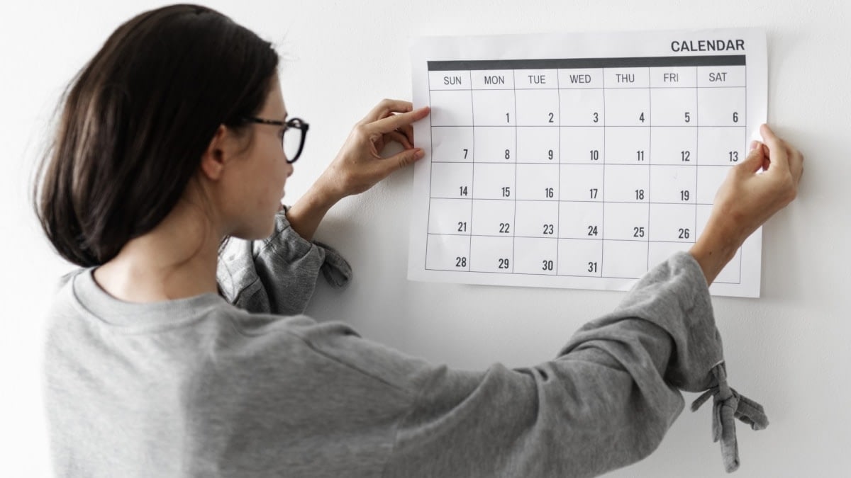 A photograph of a woman hanging a calendar on the wall.