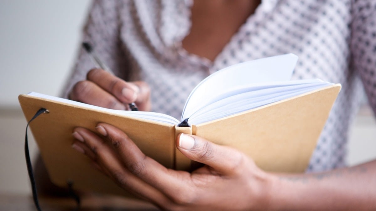 A photograph of a person writing in a notebook.
