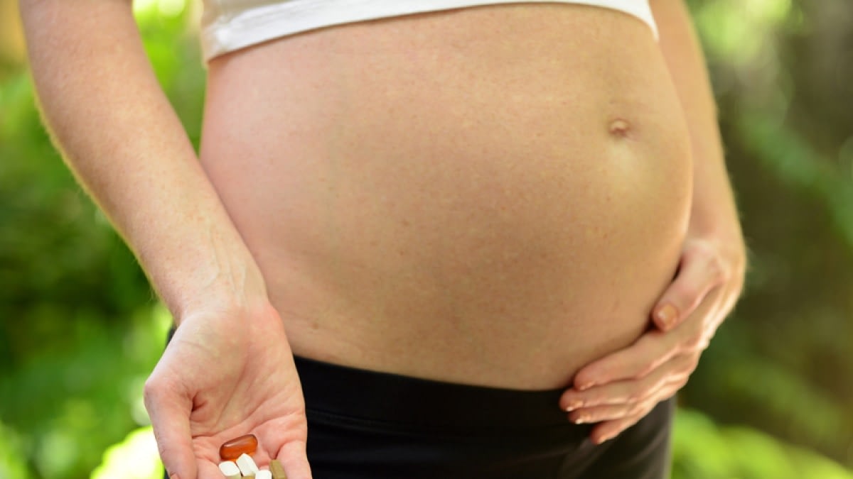 A photograph of a pregnant woman holding supplements.