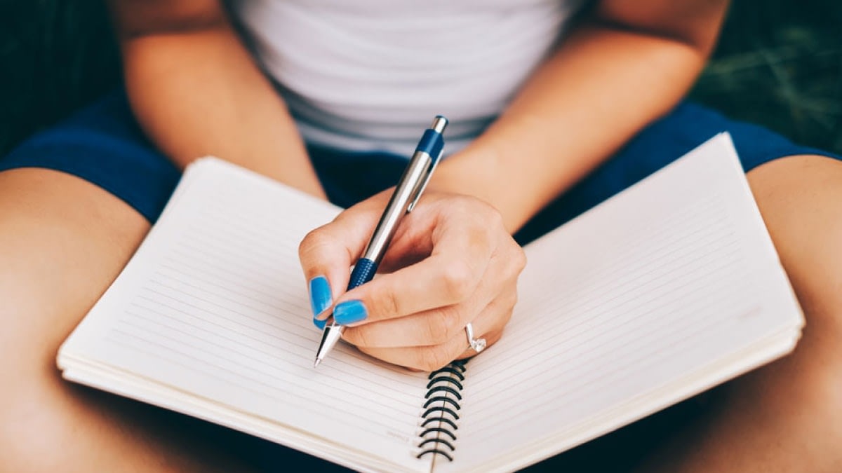 A photograph of a person writing in a notebook.