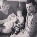 A photograph of a man, a woman holding a baby, and a small child seated on a couch.