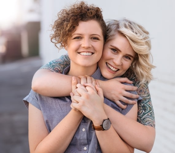 A photograph of two women hugging and smiling.