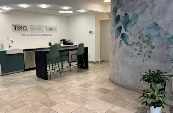 medical office with tall desk and two olive chairs, floral wall paper and trio, evolve, conceive sign on opposing wall