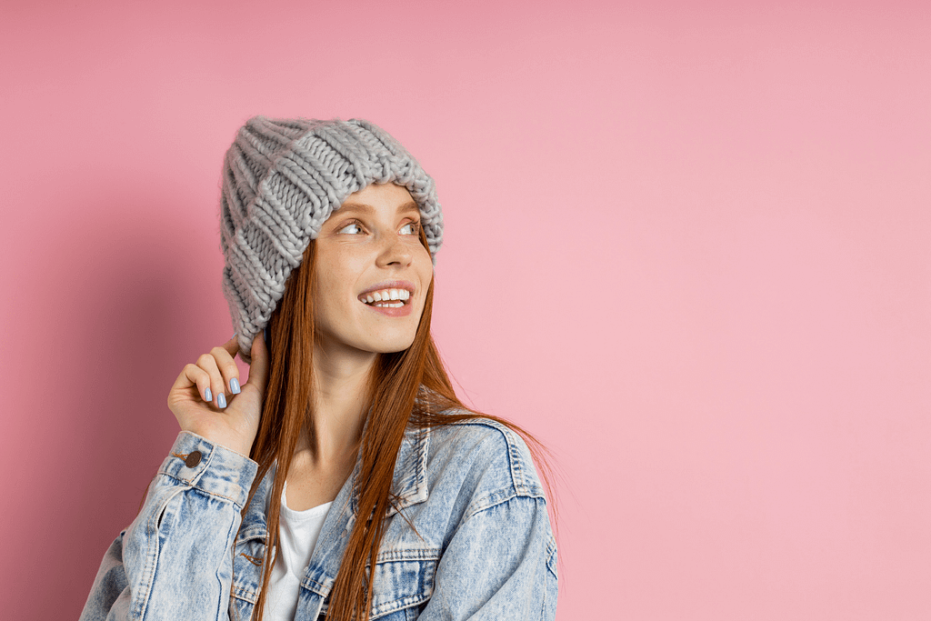 Photo with pink background of women in winter hat, with red hair looking up and smiling