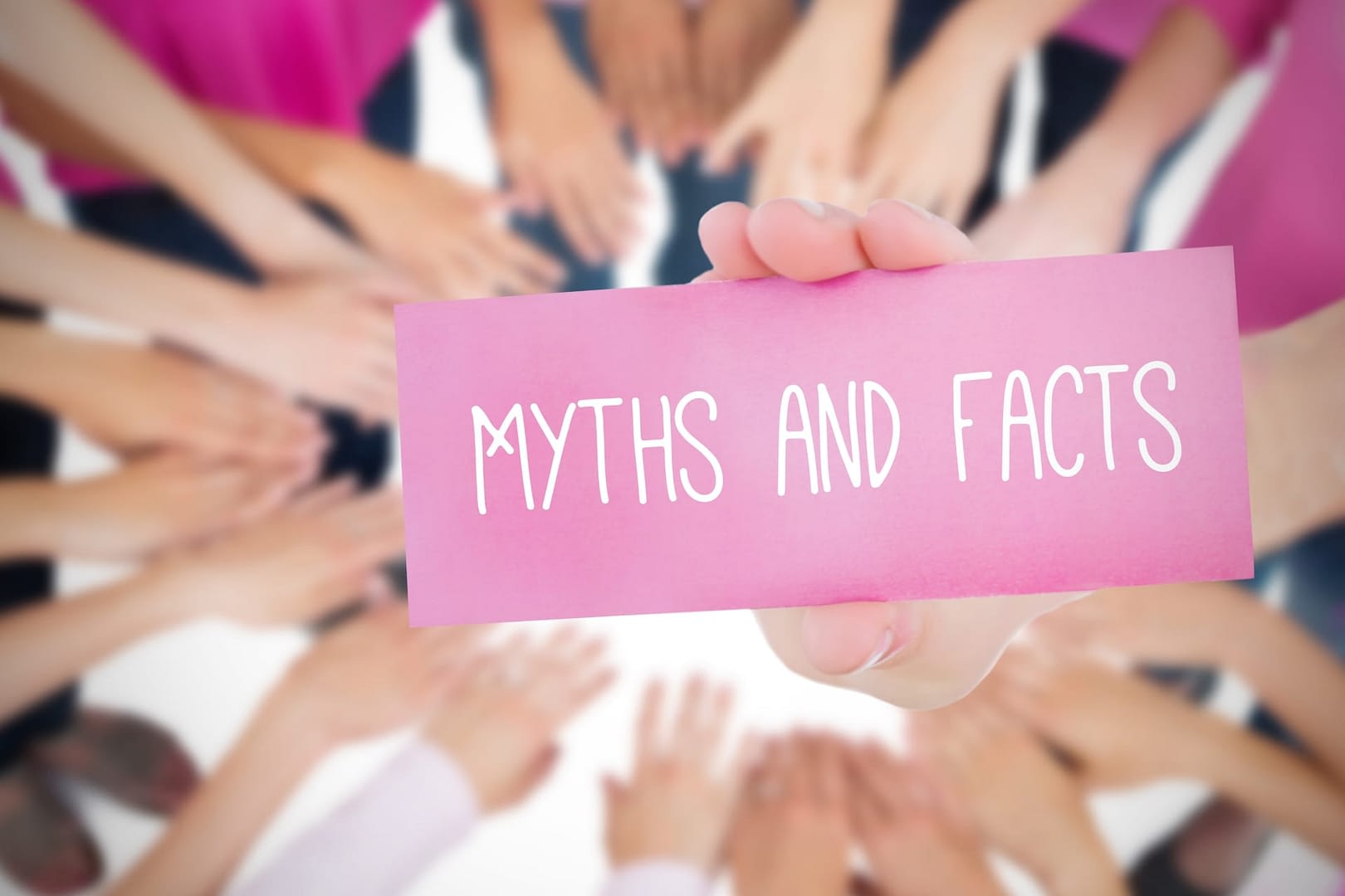 A hand holds up a sign labeled Myths and Facts. Blurred hands form in a circle in the background.