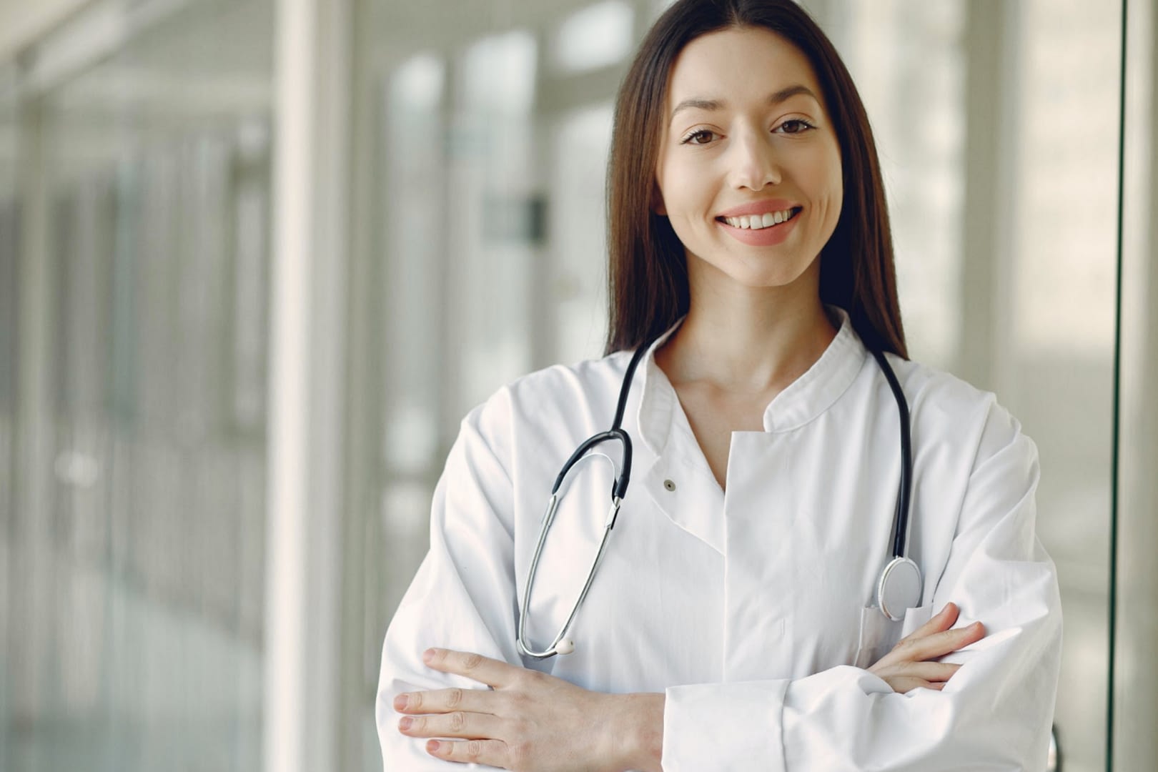 A doctor with long brown hair crossing arms in white lab coat