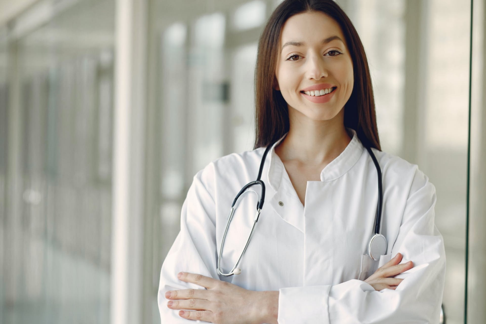 A doctor with long brown hair crossing arms in white lab coat