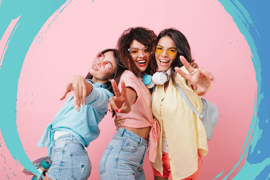 Three young women smiling and posing playfully in front of a pink background.